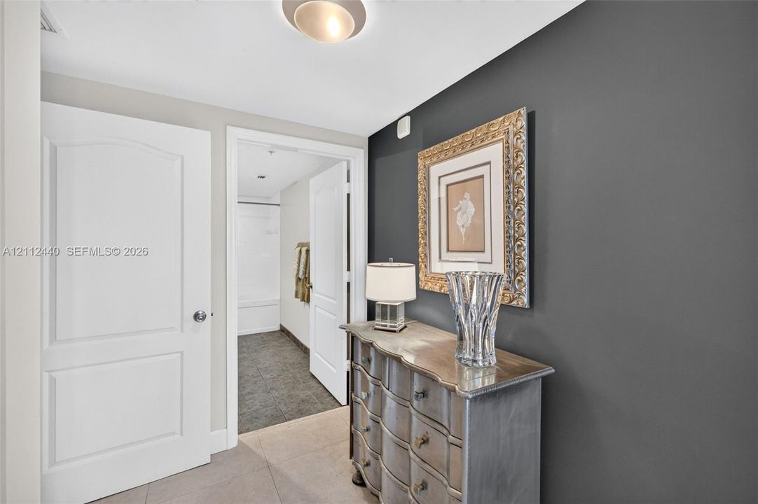 Entrance to primary bedroom and ensuite bathroom, featuring a charcoal accent wall, neutral-toned porcelain flooring, flush-mount ceiling lighting