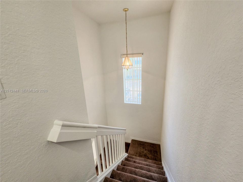 Stairwell featuring carpeted steps, white baluster railing, and a geometric pendant light fixture