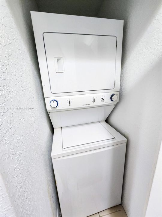 Stacked white laundry appliance featuring a top-loading washer and a dryer with manual rotary control dials