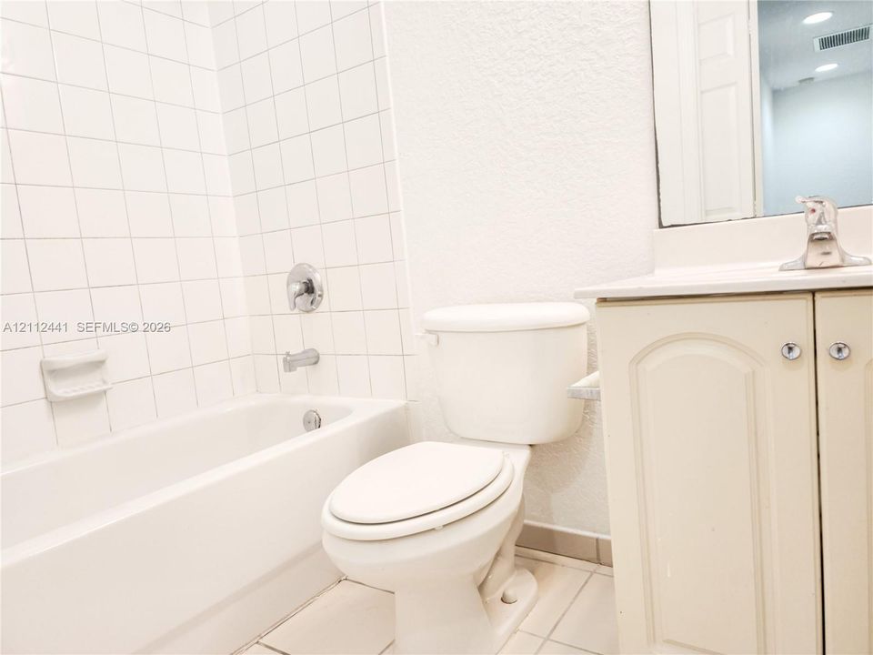 Bathroom featuring a white vanity cabinet with an integrated sink and chrome faucet, a bathtub with a white tile surround, and a wall-mounted mirror