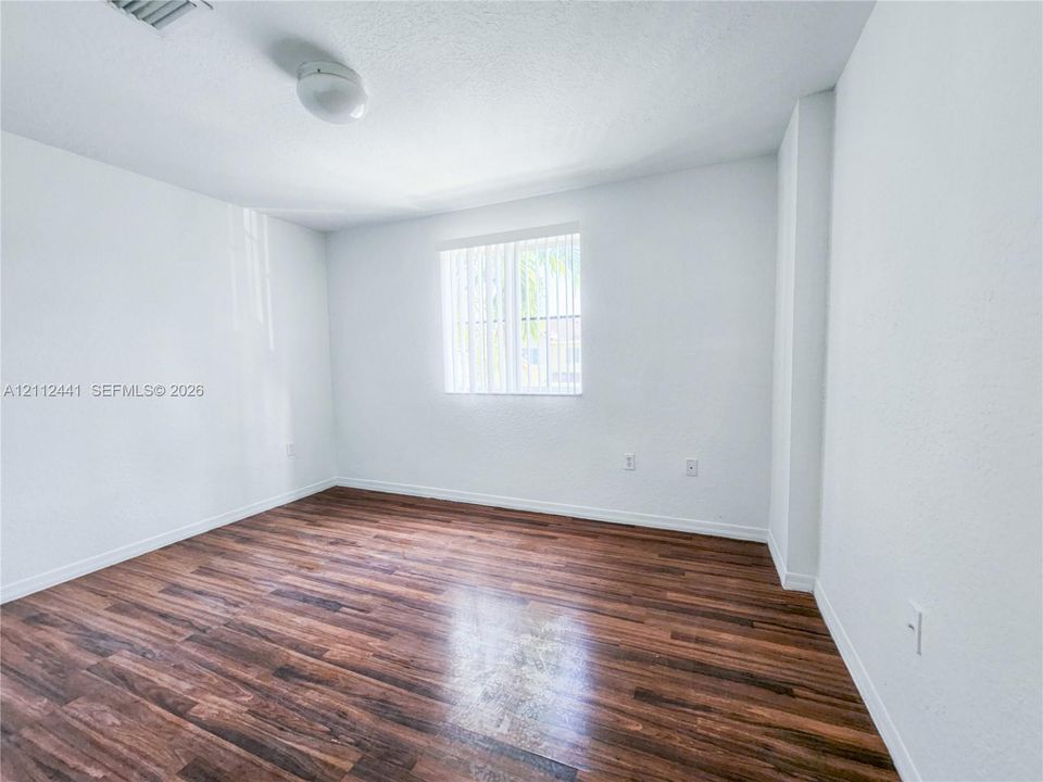 Room featuring wood-finish flooring, white walls, and a single window with vertical blinds