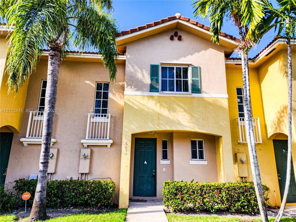 Stucco exterior featuring dual-tone paint, decorative window shutters, metal balcony railings, and a tile roof