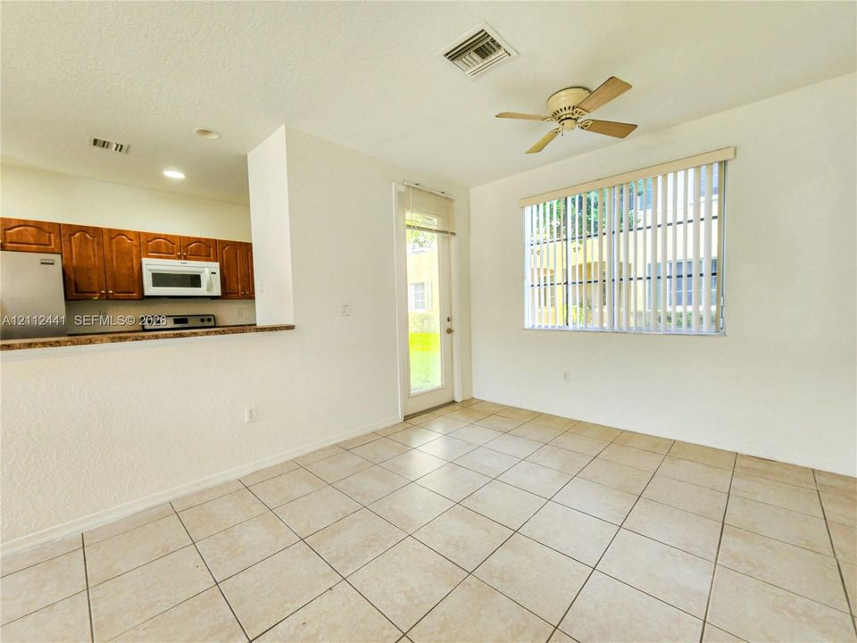 Kitchen area featuring wood cabinetry, stone-finish countertops, stainless steel appliances, neutral tile flooring, and a ceiling fan