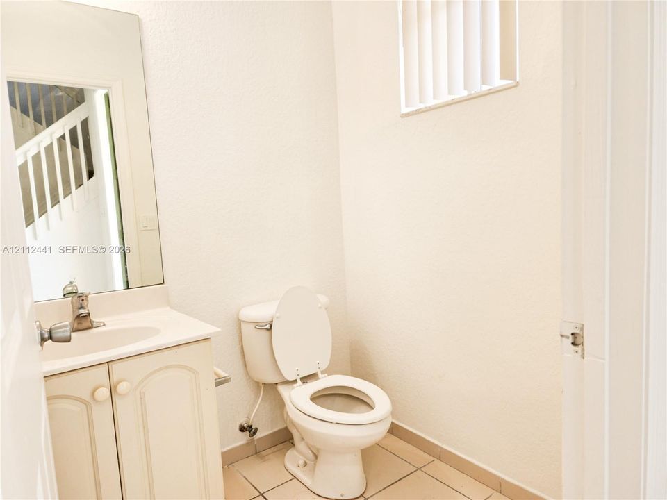 Vanity featuring cabinet storage and a sink basin, white toilet, wall-mounted mirror, and tile flooring