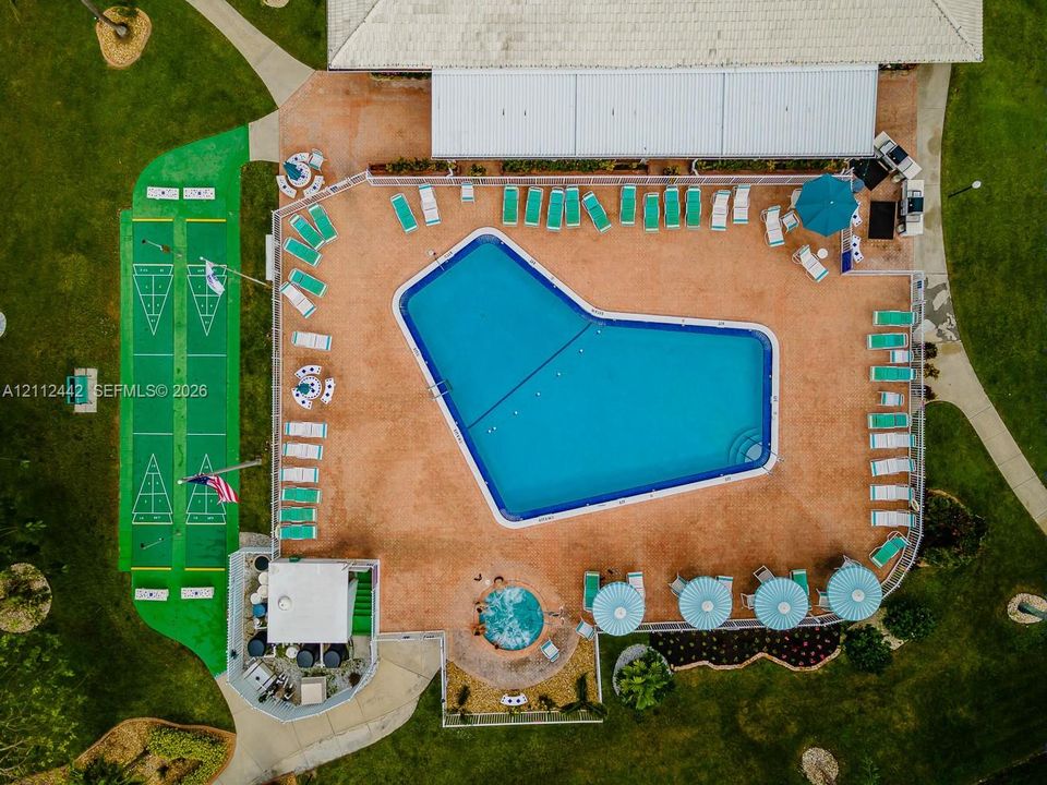 Aerial view featuring an expansive swimming pool, an integrated circular spa, a dual-lane shuffleboard court, a concrete pool deck, and a fenced perimeter