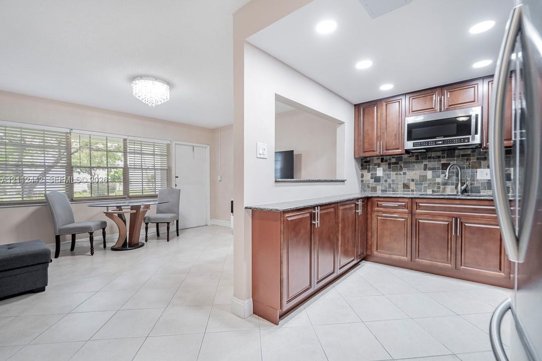 Kitchen featuring wood cabinetry, stone-style mosaic tile backsplash, stone countertops, recessed lighting, and large-format tile flooring