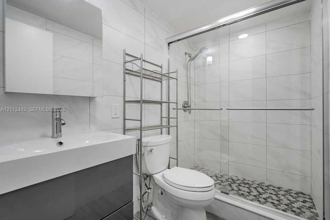Bathroom featuring a vanity with an integrated rectangular sink, wall-mounted mirror, glass-enclosed shower with a handheld fixture, and tiled surfaces