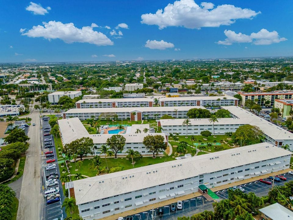 Aerial perspective of a multi-building residential complex featuring a central courtyard, a swimming pool, mature landscaping, and dedicated surface parking