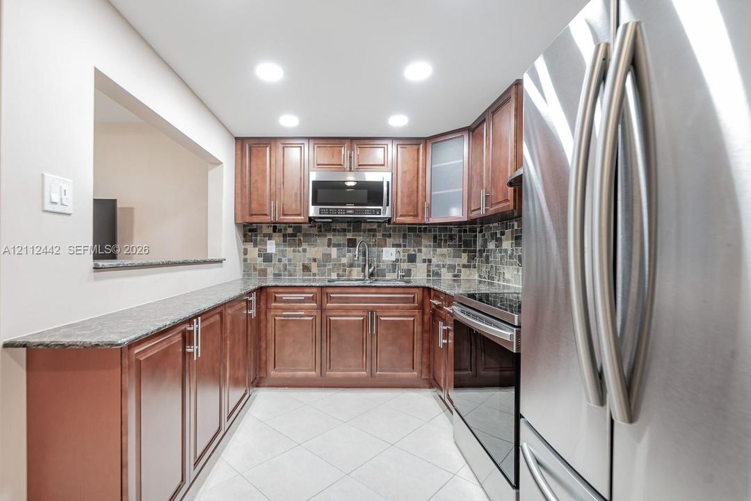 Kitchen featuring stained wood cabinetry, stone-finish countertops, mosaic tile backsplash, recessed lighting, and stainless steel appliances
