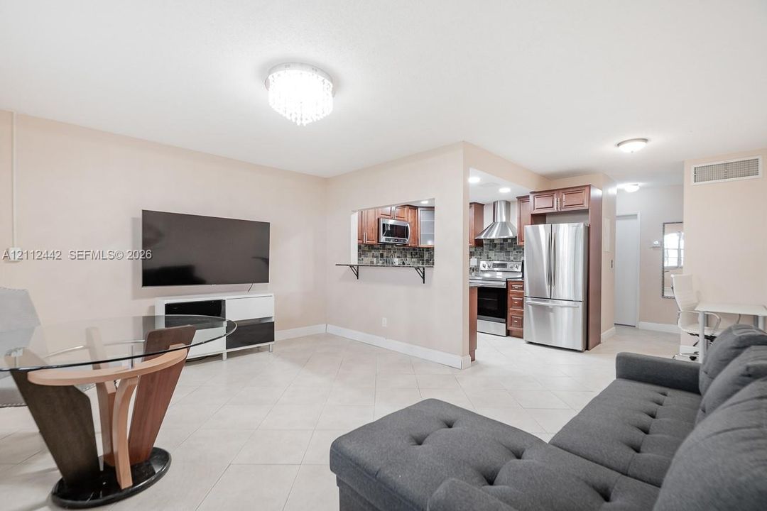 Open-concept living space featuring ceramic tile flooring, built-in breakfast bar pass-through, stainless steel kitchen appliances, and decorative flush-mount ceiling lighting