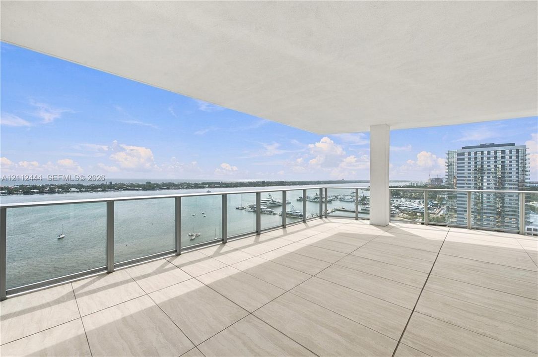 Expansive covered balcony featuring large-format stone-finish tile flooring and a glass-paneled railing with brushed metal trim