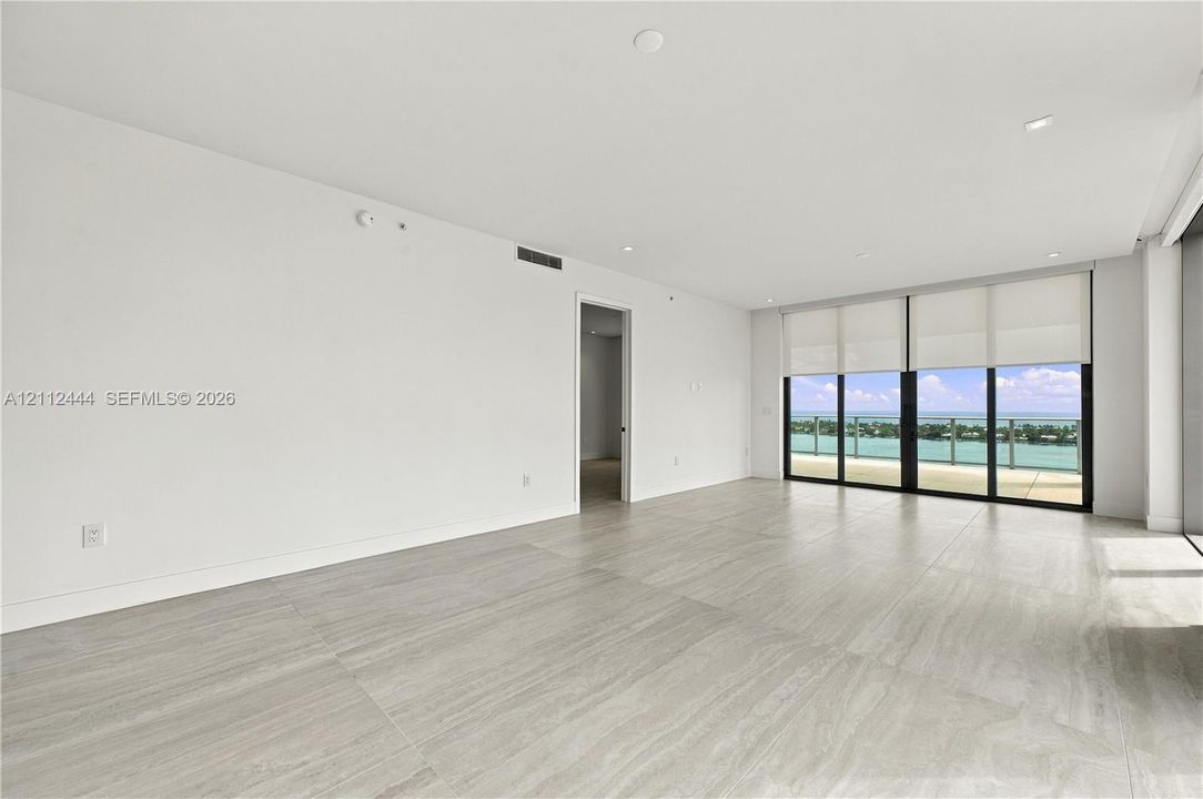 Neutral-toned stone flooring, recessed ceiling lighting, floor-to-ceiling glass sliding doors, and private exterior balcony
