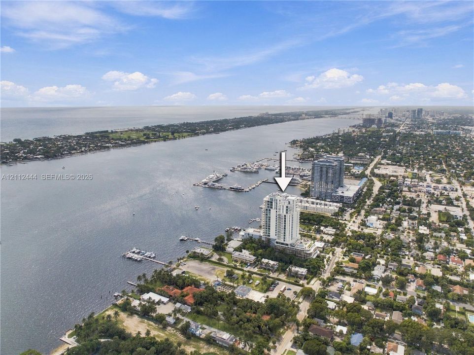 Aerial perspective of a high-rise tower situated on a coastal waterfront featuring direct proximity to a marina and expansive water scenery