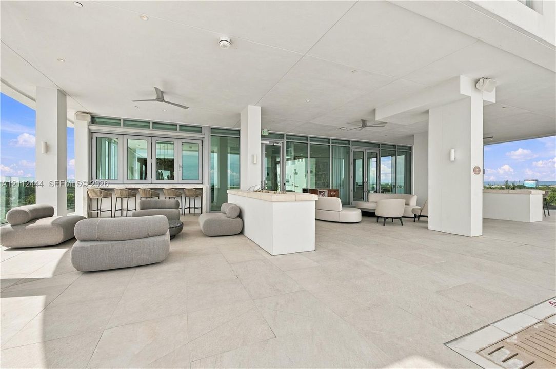Covered terrace featuring large-format stone tile flooring, built-in stone bar counter, floor-to-ceiling glass paneling, and ceiling-mounted fans