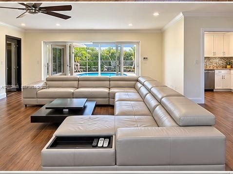 Open-concept living space featuring wood-finish flooring, recessed lighting, ceiling fan, and multi-panel sliding glass doors providing access to an enclosed pool area