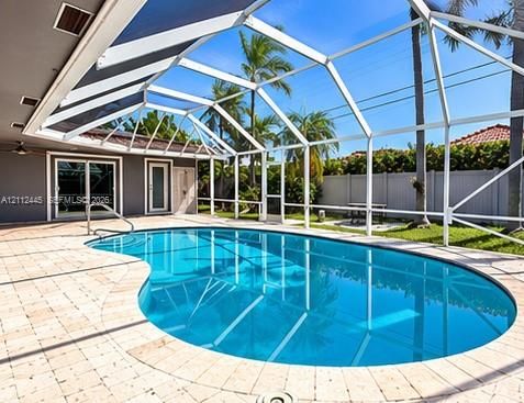 Screen-enclosed swimming pool with a concrete paver deck, metal pool cage, and privacy fencing