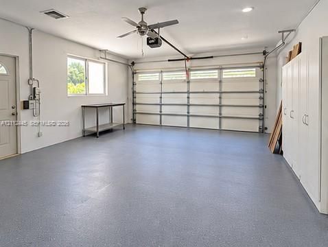 Spacious garage featuring a durable epoxy floor finish, wall-mounted storage cabinetry, recessed lighting, and a ceiling fan