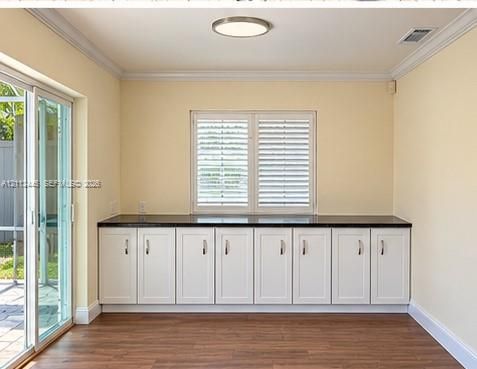Custom built-in white cabinetry featuring dark stone-finish countertops, wood-finish flooring, sliding glass door, and window with plantation-style shutters