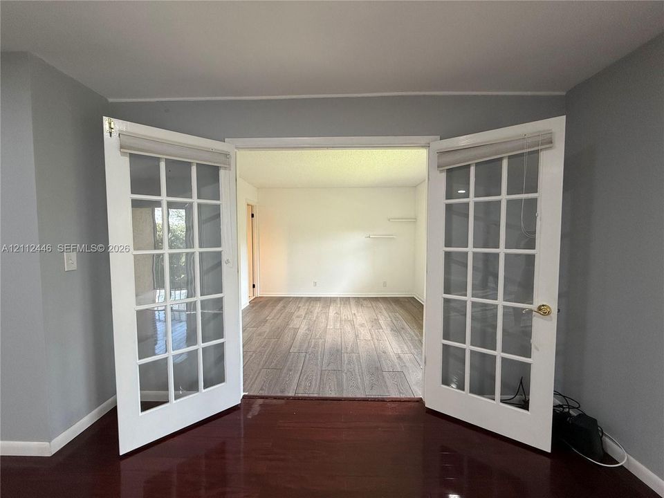 Double glass-paned doors featuring white frames, brass-finish hardware, and built-in blind fixtures, accented by wood-finish flooring