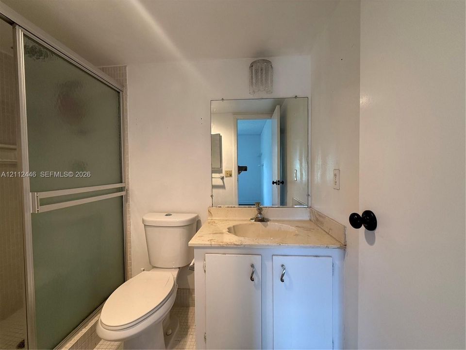 Bathroom featuring a stone-surface vanity with an integrated basin, a shower enclosure with a frosted sliding glass door, a wall-mounted mirror, and a crystal-style light fixture