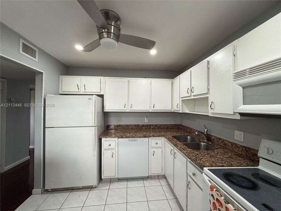 Kitchen featuring white cabinetry, stone-surface countertops, dual-basin stainless steel sink, tile flooring, and a ceiling-mounted fan