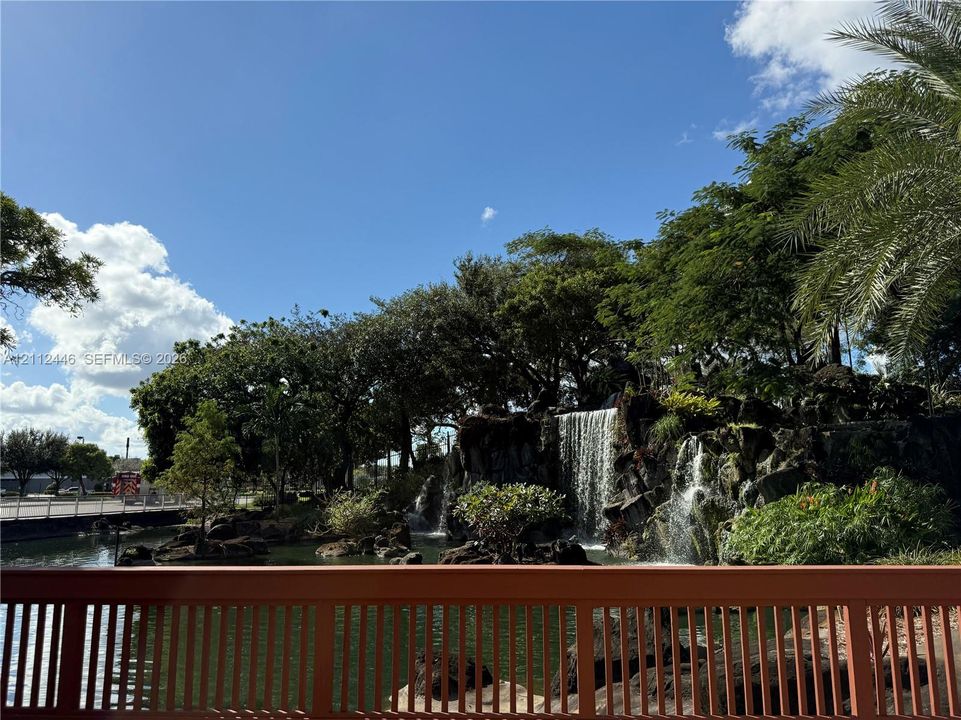 Custom rock-scaped waterfall with tiered water features, built-in stone retaining wall, mature landscaping, and an ornamental metal railing overlooking the water