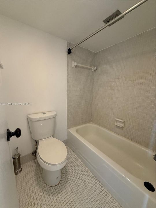 Bathroom featuring a white bathtub, small-format tile flooring, wall-mounted shower curtain rod, and integrated soap dish