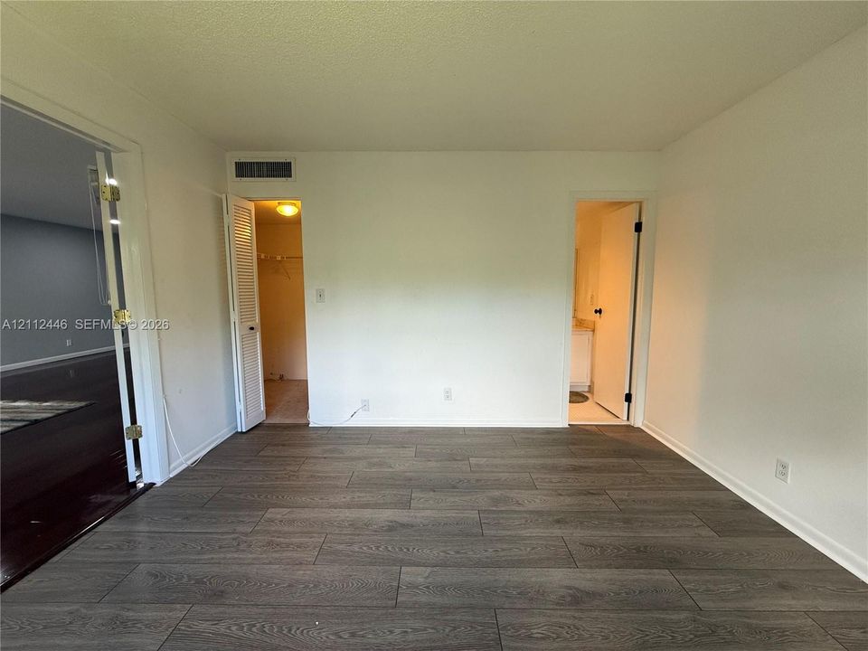 Neutral-toned interior space featuring wood-finish flooring, two doorway entries, a louvered closet door, and a textured ceiling