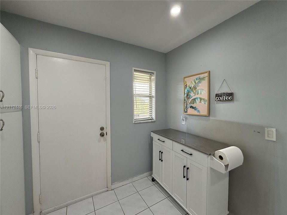 White cabinetry featuring dark hardware and a solid surface countertop, tile flooring, and a single-panel door