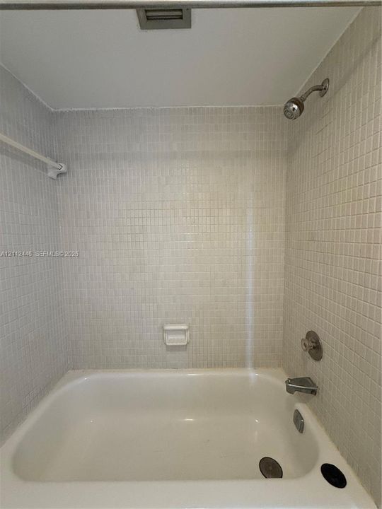 Bathtub featuring a white finish, wall-mounted shower head, integrated faucet, built-in soap dish, and neutral mosaic tile surround
