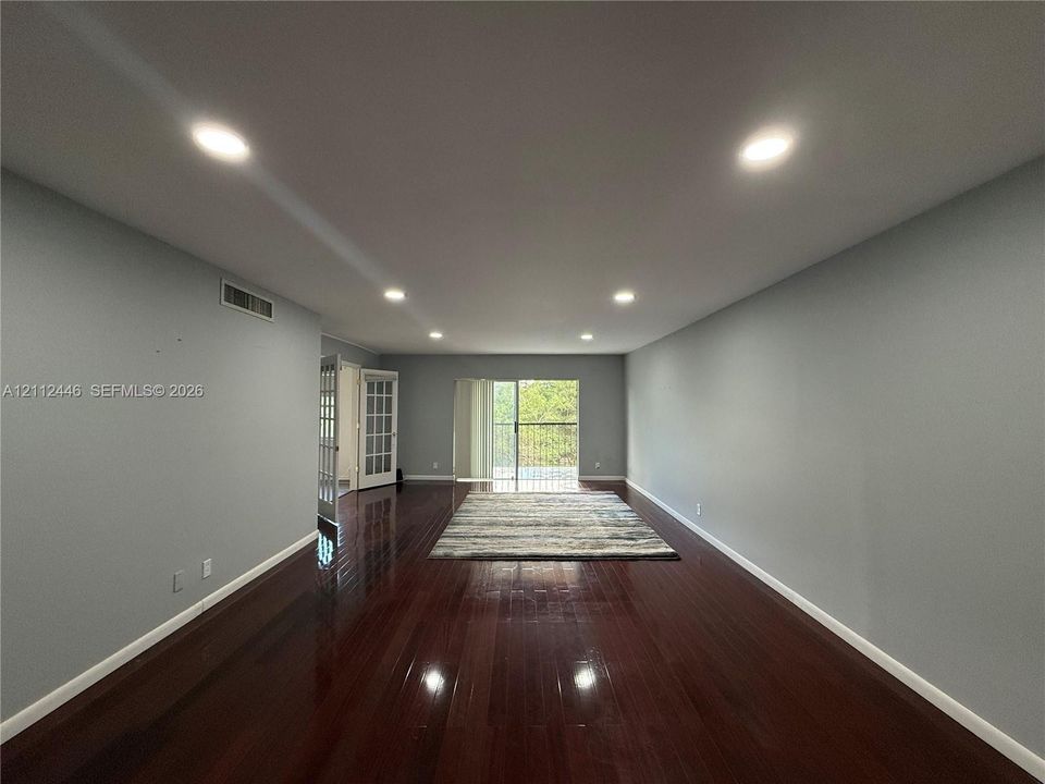 Interior room featuring dark wood-finish flooring, recessed lighting, and a glass-paneled sliding door opening to a balcony