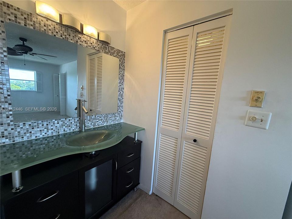 Black vanity featuring a glass vessel sink, chrome single-lever faucet, tiled mirror surround, and louvered bi-fold closet doors
