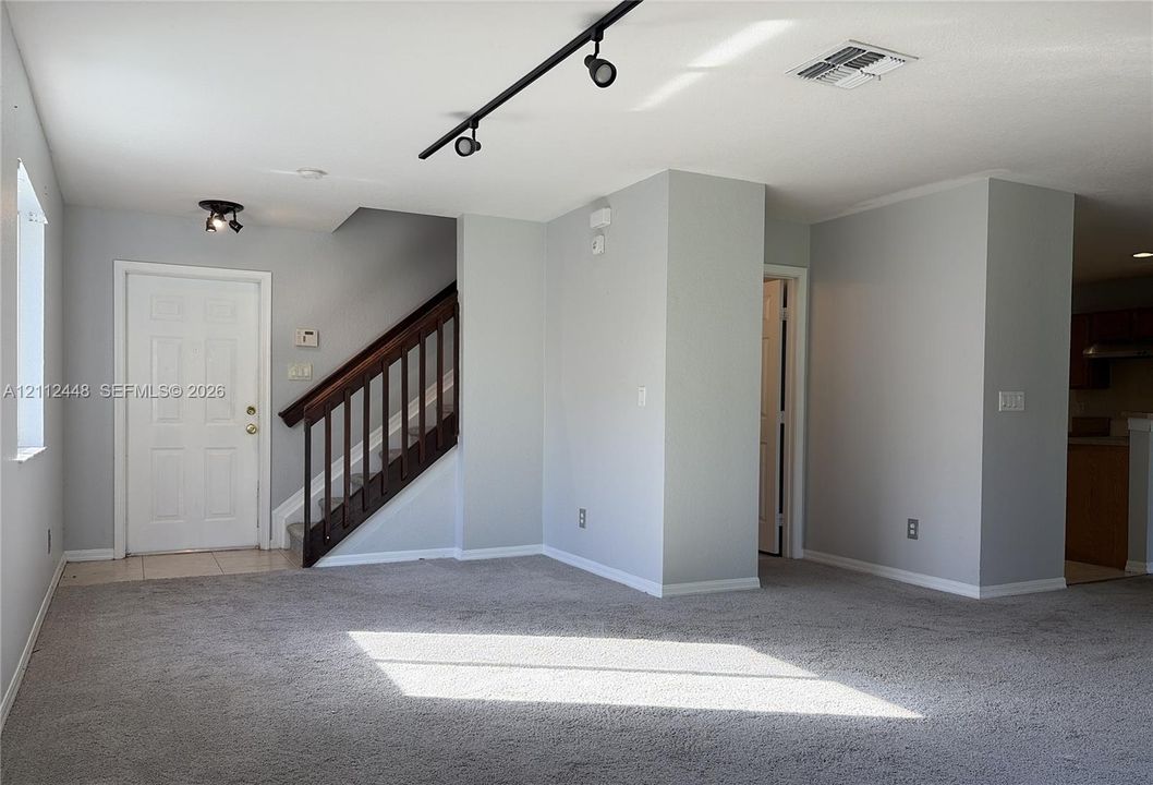 Interior space featuring neutral-toned wall paint, neutral carpeting, track lighting, and a staircase with a dark wood railing