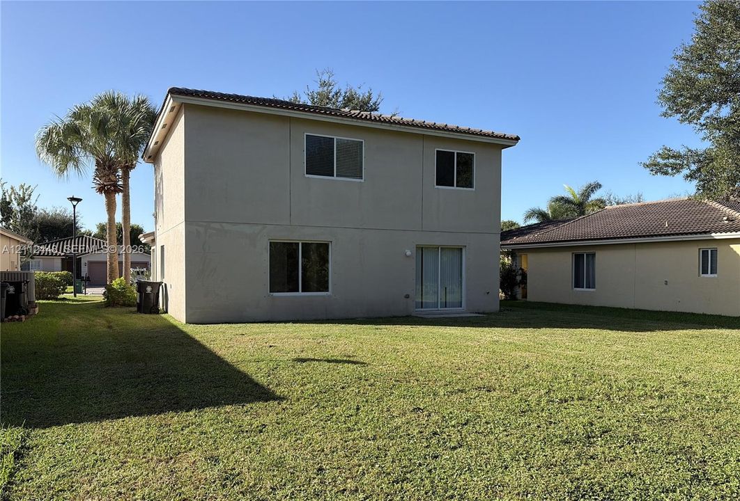 Two-story exterior featuring a neutral stucco facade, tile roofing, sliding glass door, and an expansive lawn