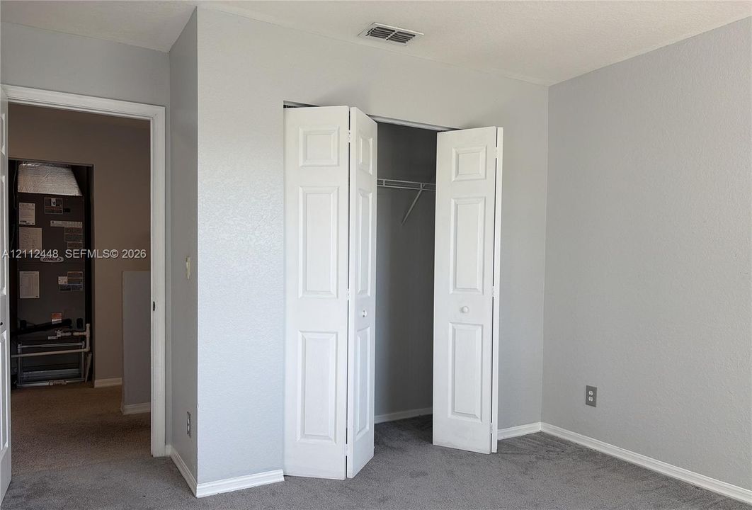 Neutral-toned walls paired with gray carpeting and a closet featuring white paneled bifold doors and built-in shelving
