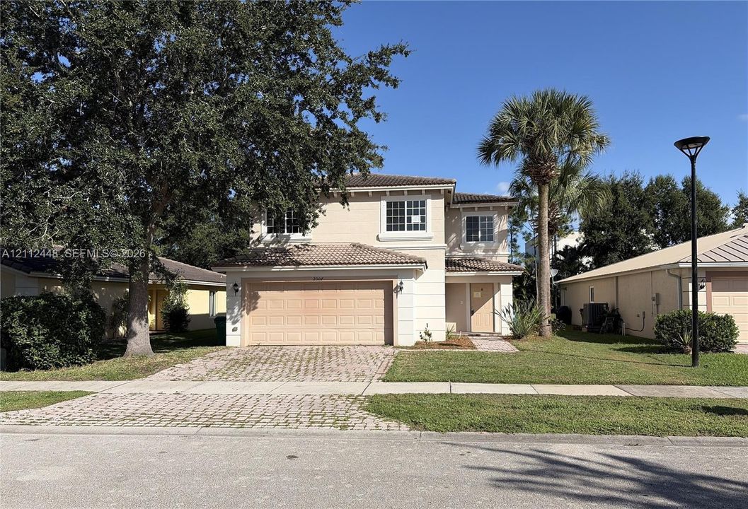 Two-story stucco exterior featuring a tiled roof, an attached two-car garage, a paved driveway, and mature landscaping