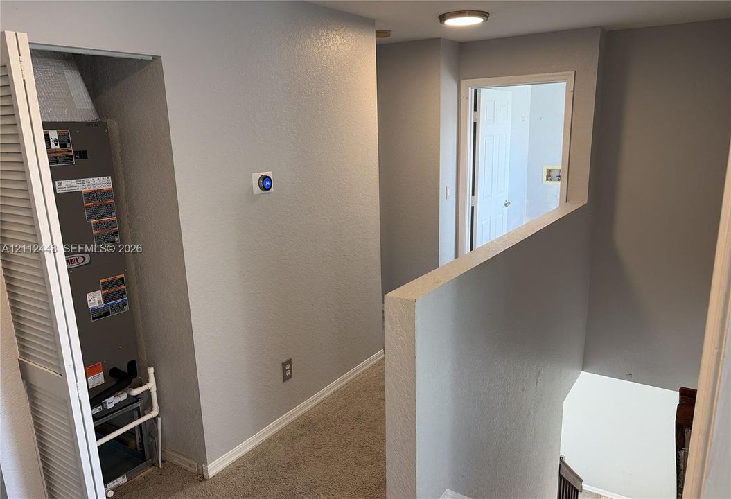 Interior hall featuring a digital programmable thermostat, louvered closet door concealing mechanical systems, and flush-mount ceiling lighting