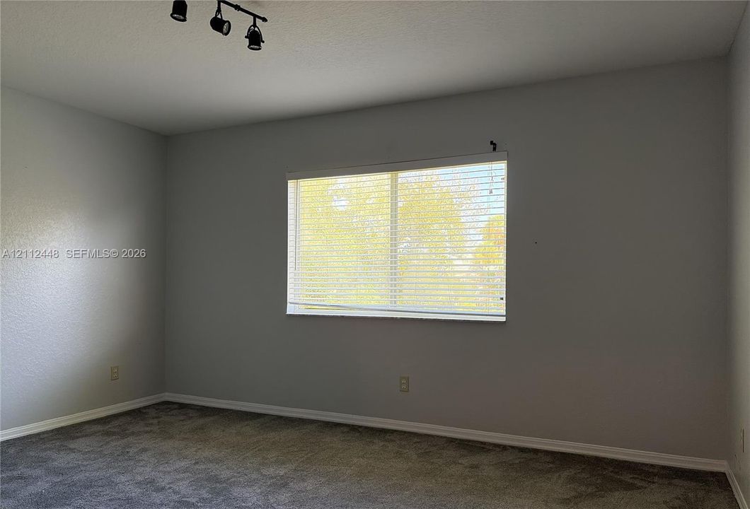 Neutral-toned walls, wall-to-wall carpet, single-pane window with horizontal blinds, and three-bulb adjustable track lighting