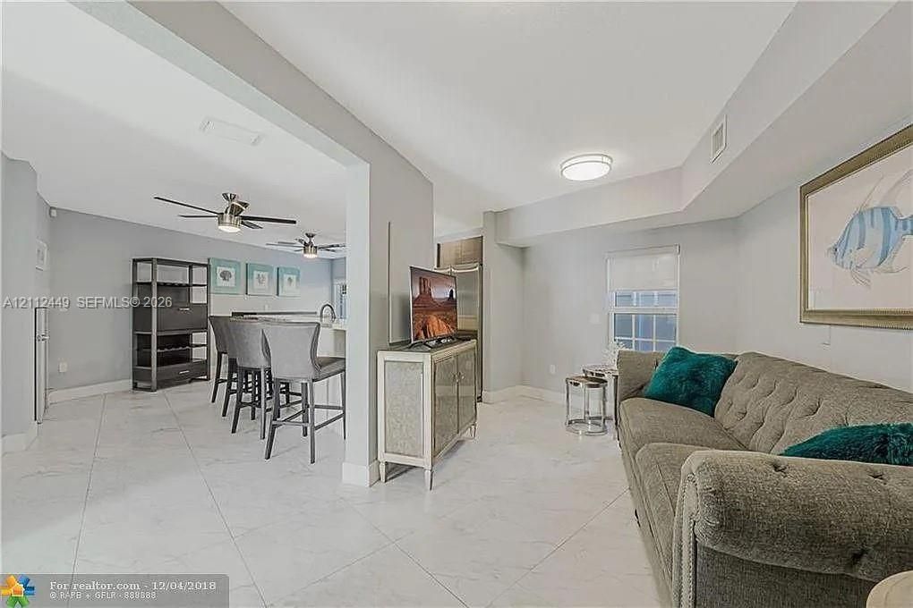 Open interior featuring light-colored tile flooring, flush-mount ceiling lighting, ceiling fans, and a kitchen peninsula