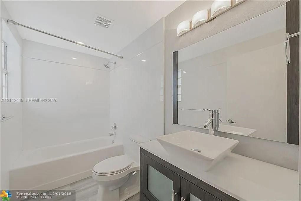 Dark wood-finish vanity with a rectangular vessel sink, topped by a sleek polished faucet, set against a large wall-mounted mirror with integrated lighting