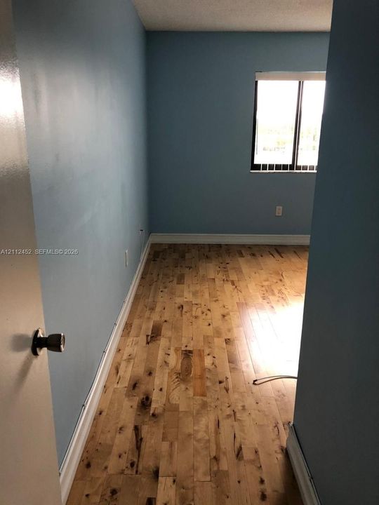 Room featuring wood-finish flooring, a single window, and solid interior door with a brushed metal handle