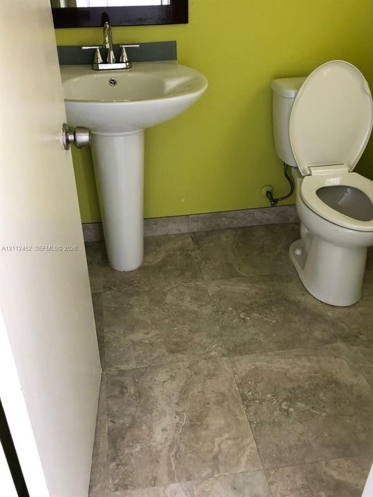 White pedestal sink with chrome faucet, stone-finish tile flooring, and a two-piece porcelain toilet