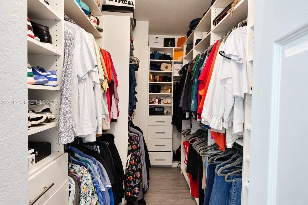 Custom walk-in closet featuring extensive white built-in shelving, integrated tiered storage, floor-to-ceiling hanging rods, and multi-drawer cabinetry