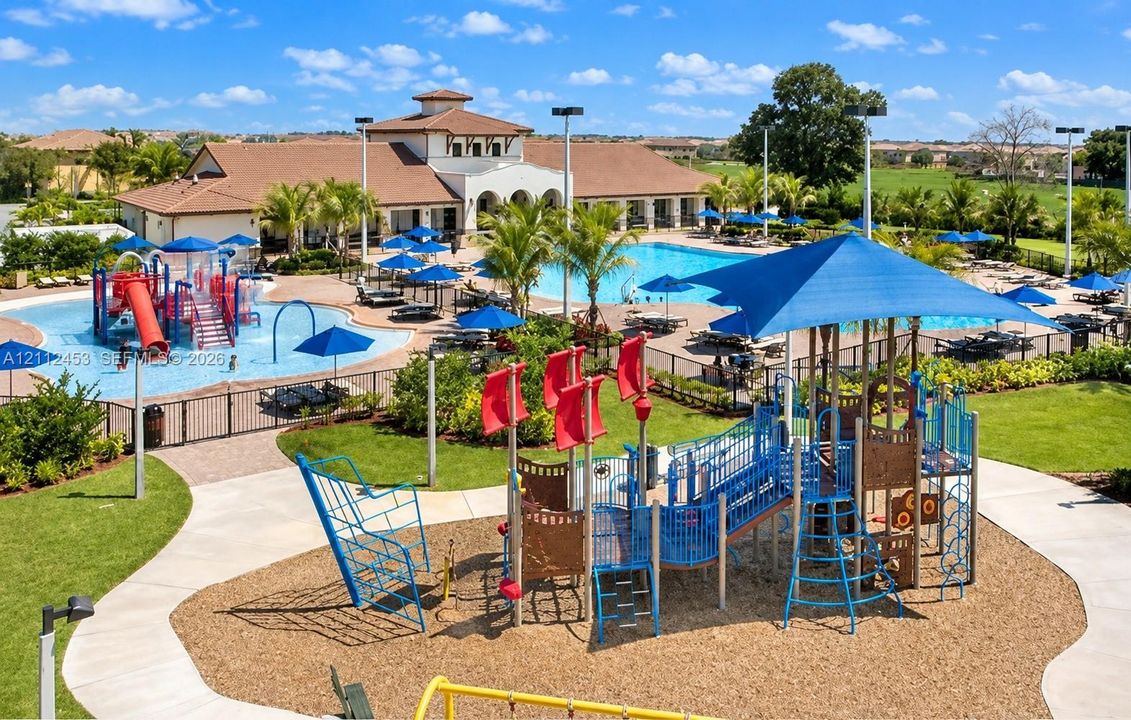 Community recreation area featuring a multi-level playground structure, aquatic center with a splash zone, paved walkways, and professional landscaping