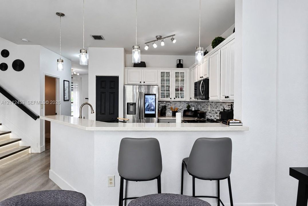 Kitchen featuring white cabinetry, stone-surface breakfast bar, glass-front upper cabinet doors, stainless steel refrigerator, and trio of pendant light fixtures
