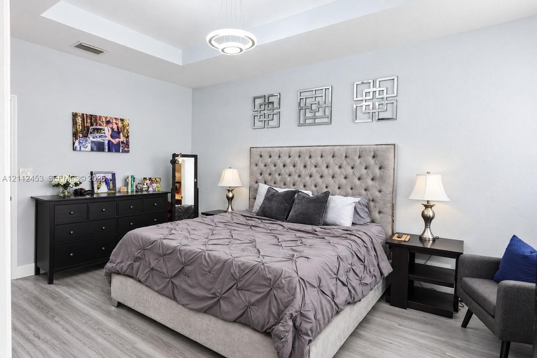 Tray ceiling featuring a contemporary circular ring light fixture, complemented by wood-finish flooring