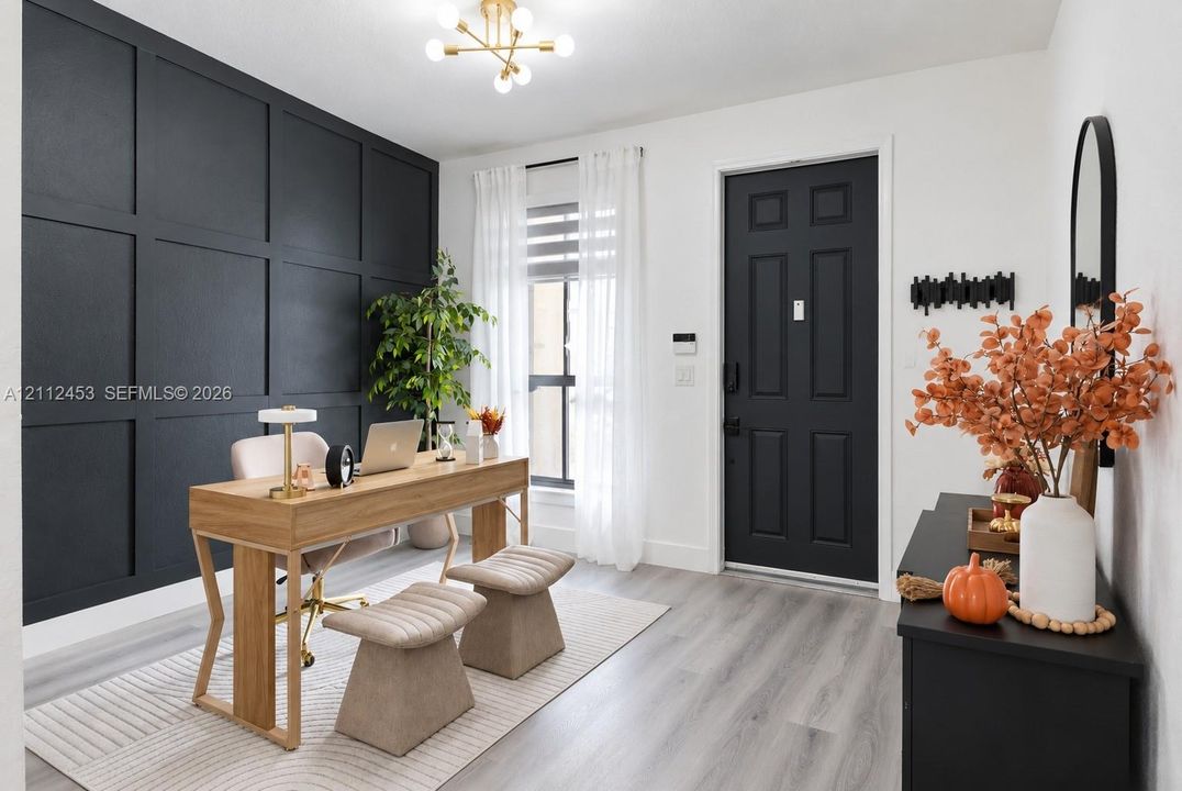 Room featuring a matte black grid-patterned accent wall, wood-finish flooring, a contemporary six-arm chandelier, and a black-finished entry door