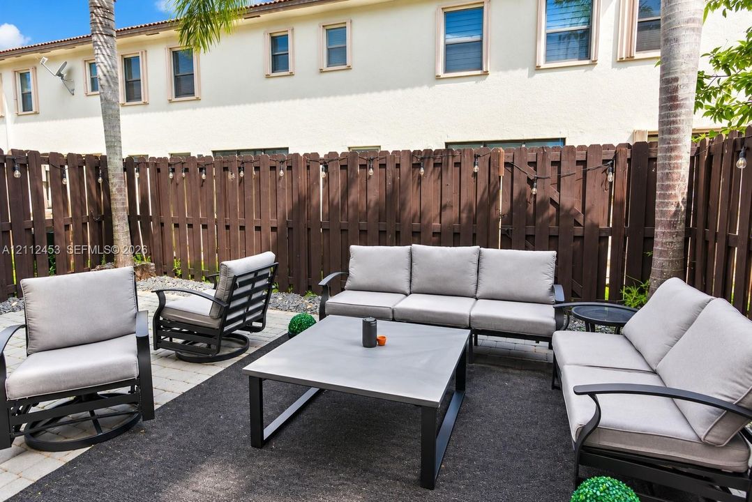 Private rear patio featuring stone paver flooring, a solid wood privacy fence, and integrated string lighting