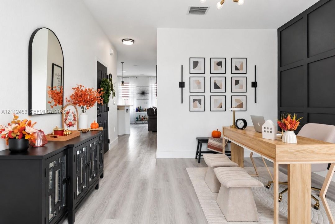 Light-toned wood-finish flooring, dramatic black accent wall with grid-style paneling, arch-top wall mirror, modern linear wall-mounted lighting, and recessed ceiling lighting