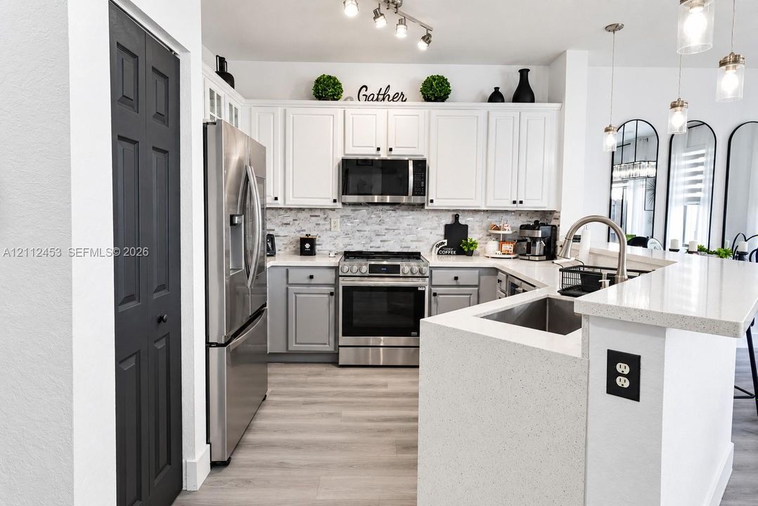 Kitchen featuring white upper cabinetry, grey lower cabinetry, light-toned stone countertops, stainless steel appliances, and wood-finish flooring